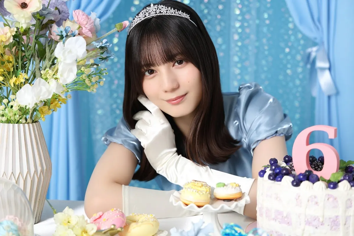 Hinakoi anniversary portrait of a performer in a blue puff-sleeved dress, tiara and white gloves beside flowers, decorated doughnuts and a berry-topped cake with a pink number six.