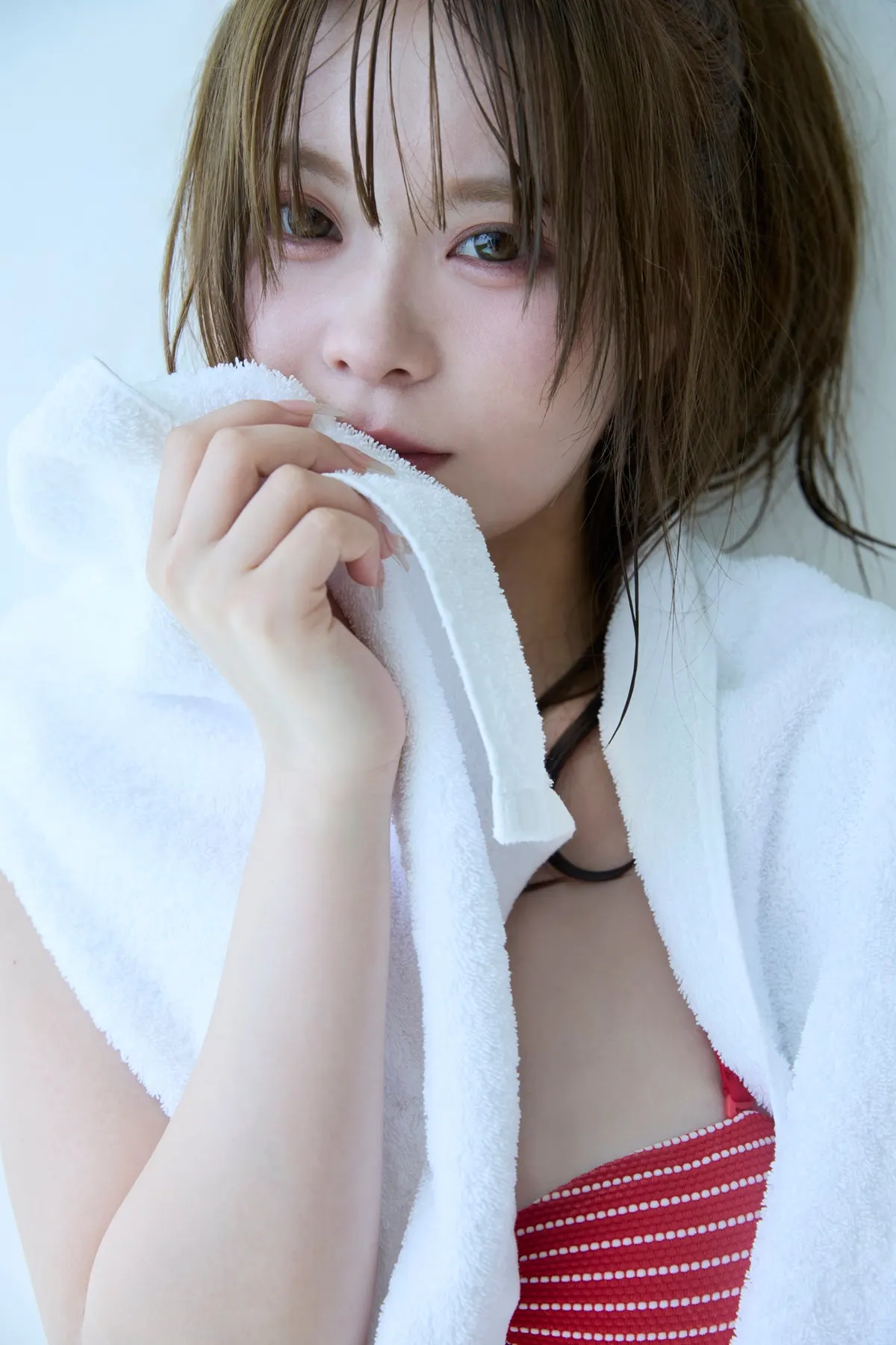 Sakura (さくら) holding a white towel near her face, with the towel draped over red-and-white striped swimwear.