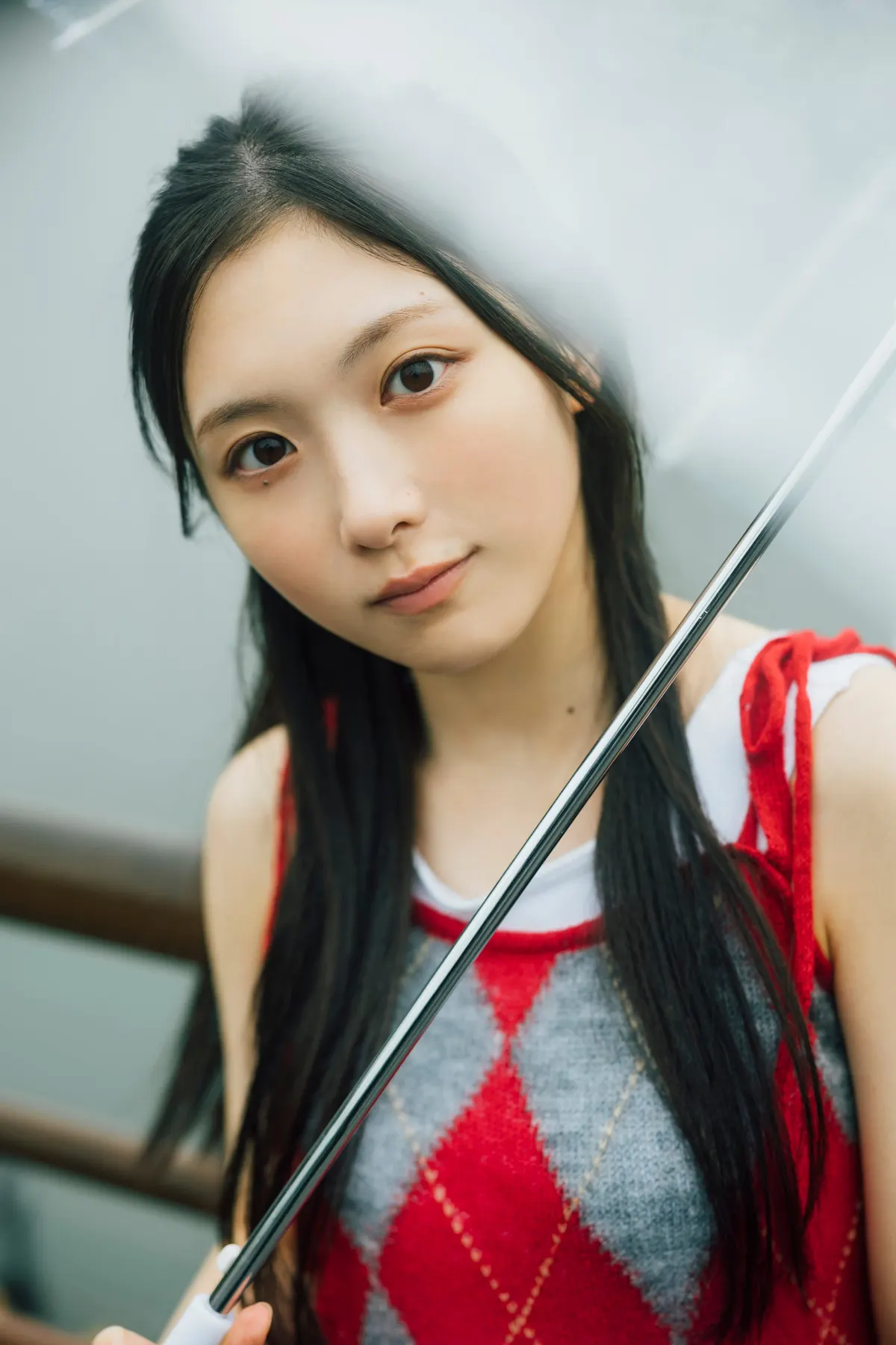 Airi Taniguchi beneath a transparent umbrella in red-and-gray argyle knitwear.