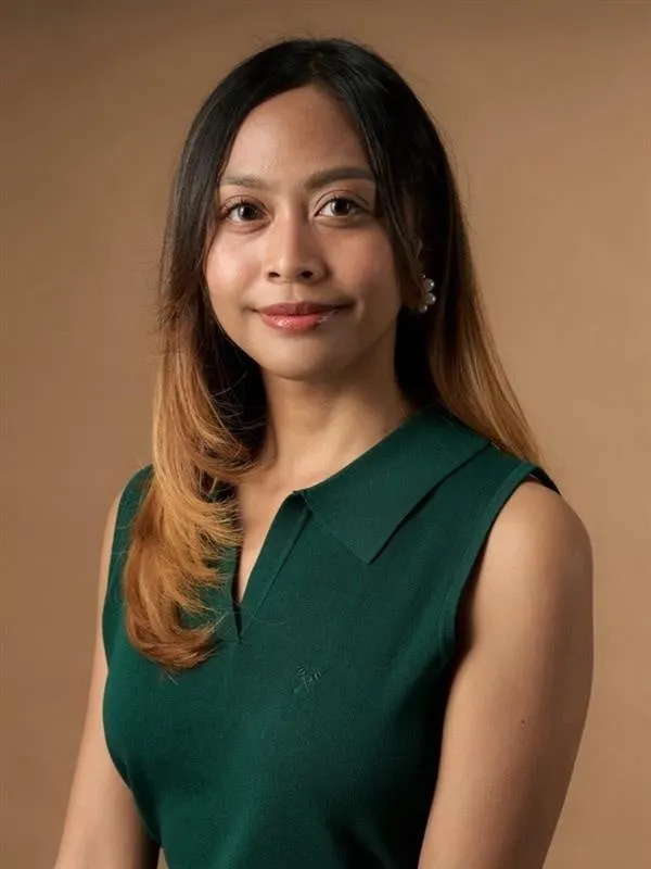 Princess Ampol wears a sleeveless green collared top against a warm brown background.