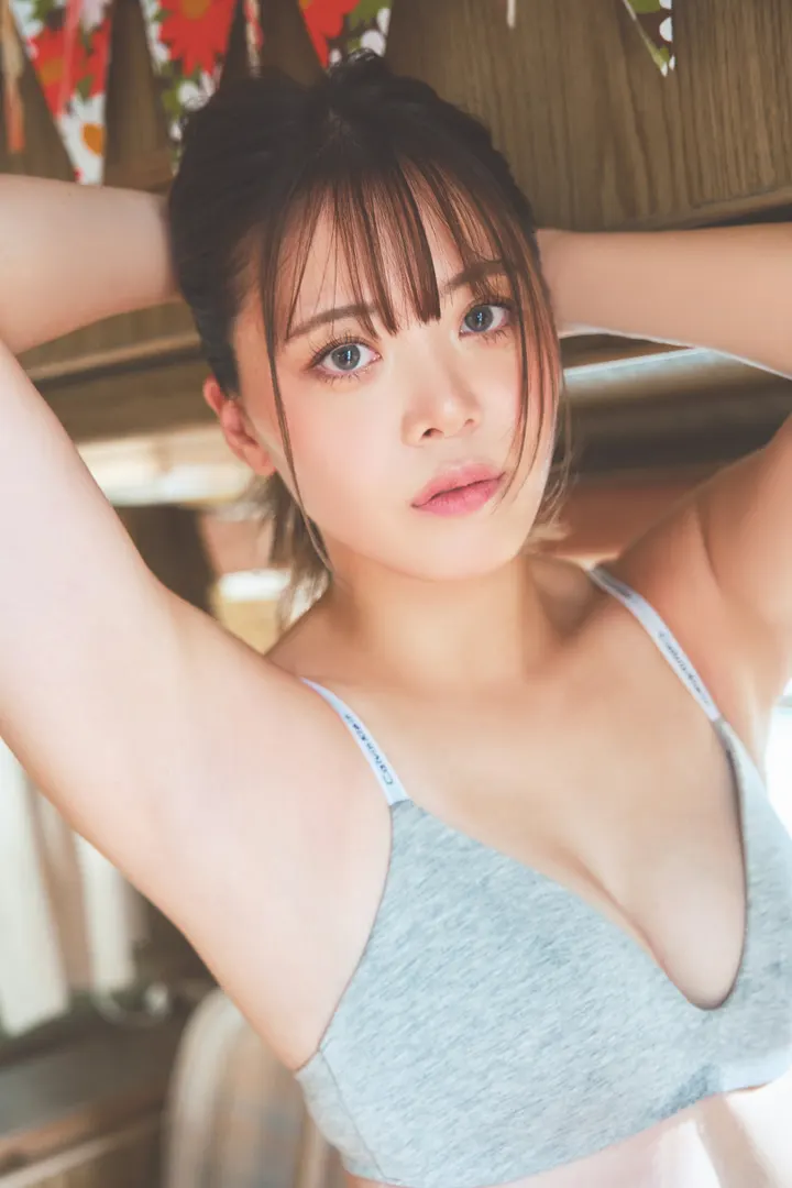 Mayu Iwatani (岩谷麻優) in a gray top with both arms raised behind her head, against a wooden interior.