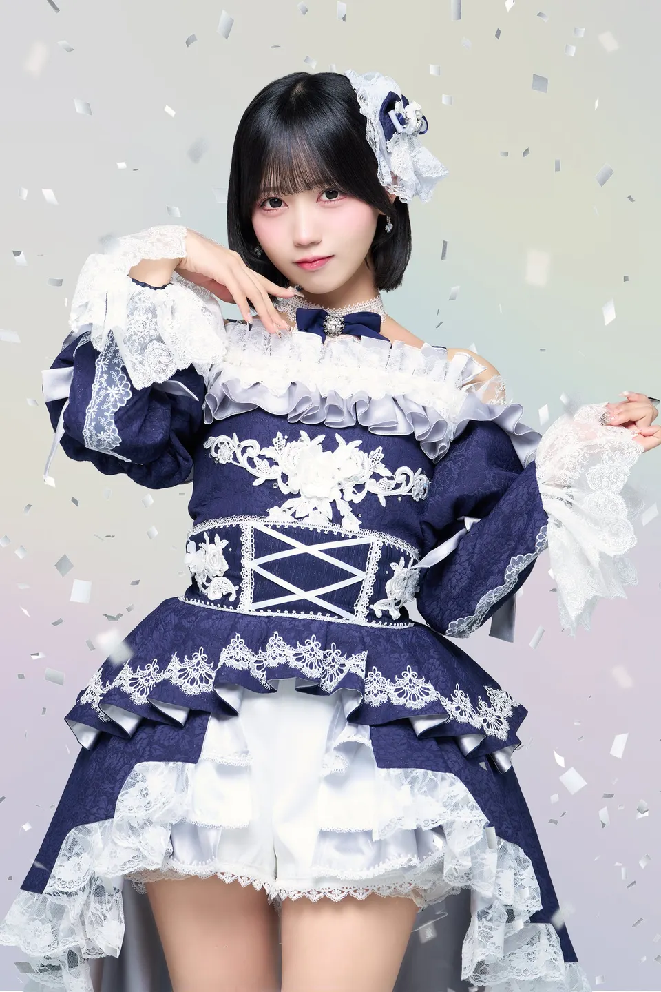 Meru Matsumoto wears a navy-and-white lace stage costume with a white hair ornament and holds one hand beneath her chin.
