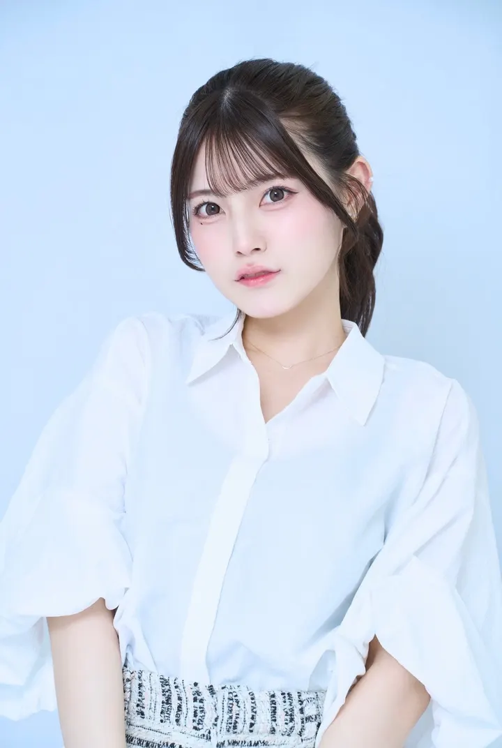 Shujinko, also known as Saki Kanamaru, wearing a white collared blouse against a pale blue background.