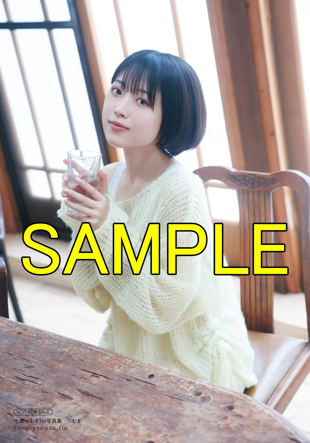 HMV bonus print sample showing Tsumugi Nanase holding a clear glass while seated at a wooden table in pale knitwear beside tall windows.
