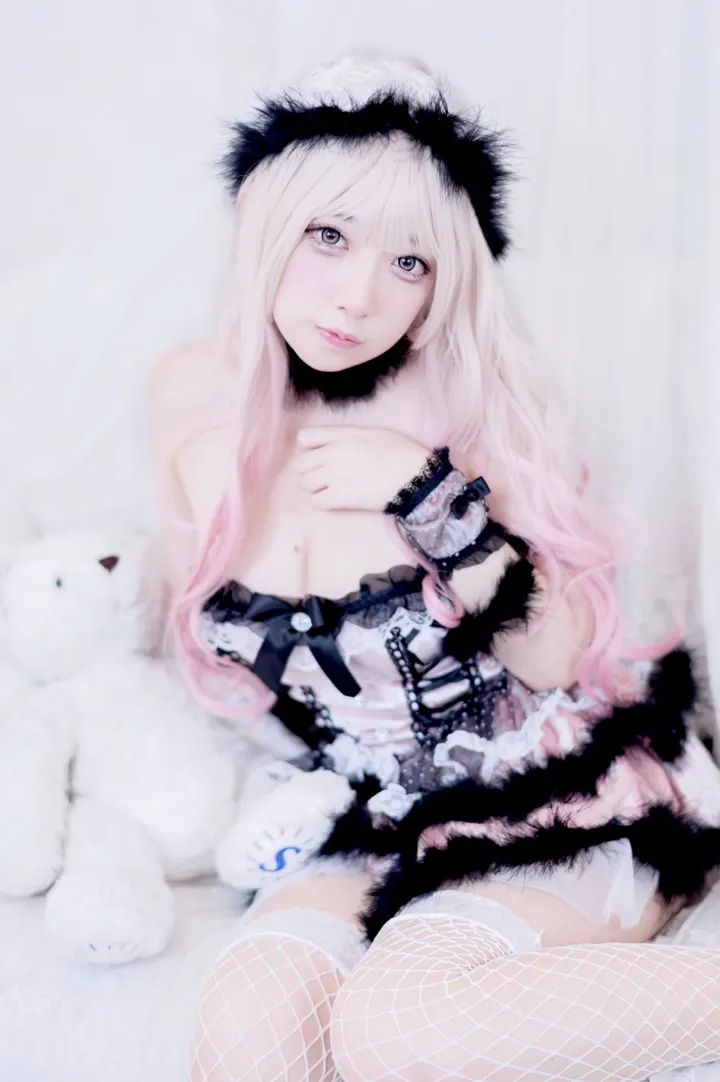 Publicity portrait of Shionomeri with long pale pink hair, black fuzzy ears and a pink-and-black costume, seated beside a white plush toy.