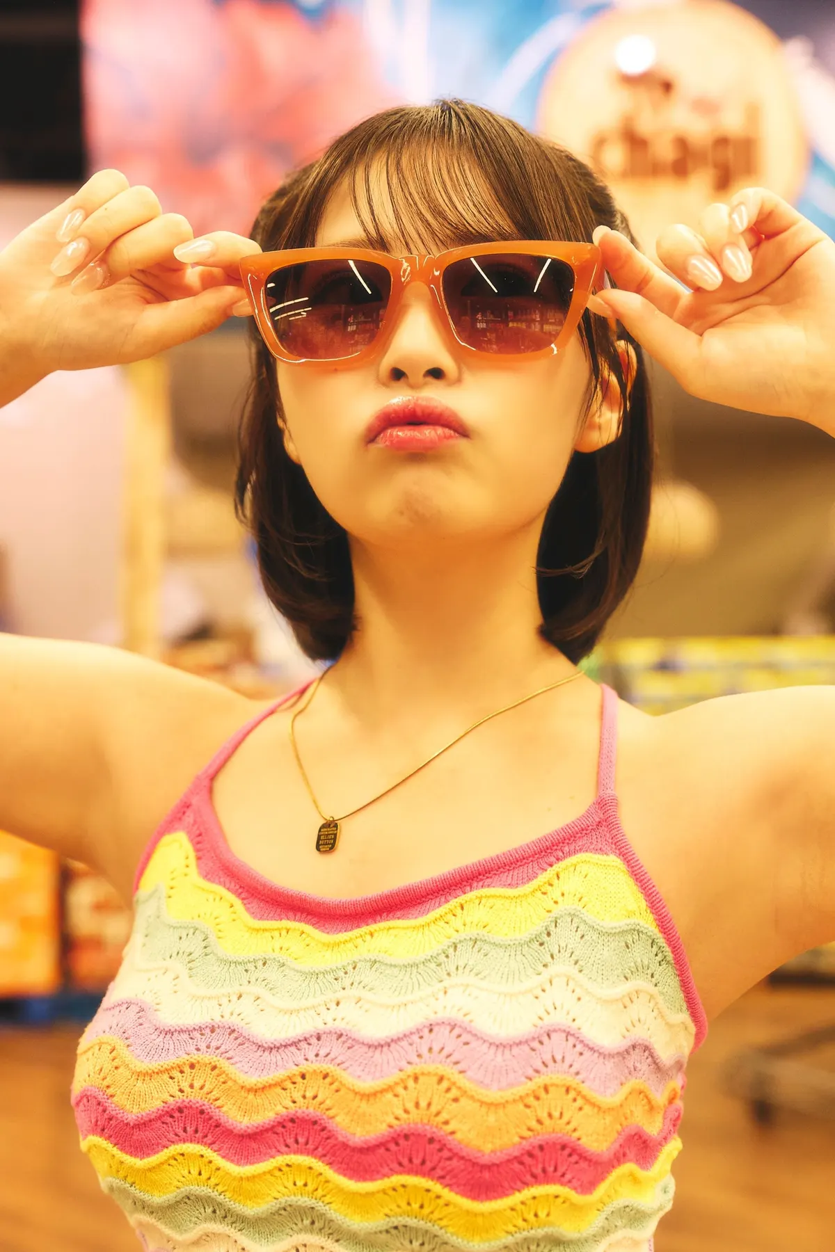 Yumeka Kimura (木村夢叶) holds the corners of her orange sunglasses while wearing a multicolored crochet top and a pendant necklace.