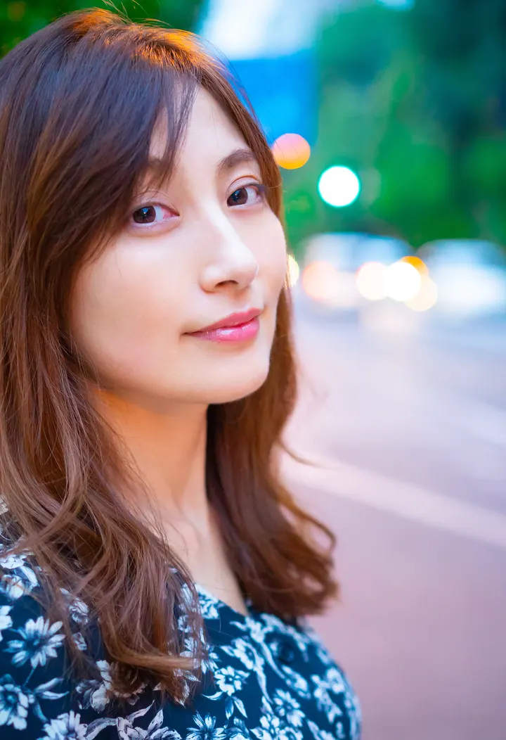 Yoko Kumada (熊田曜子) wearing a dark floral-patterned top against a softly blurred street background with greenery and lights.