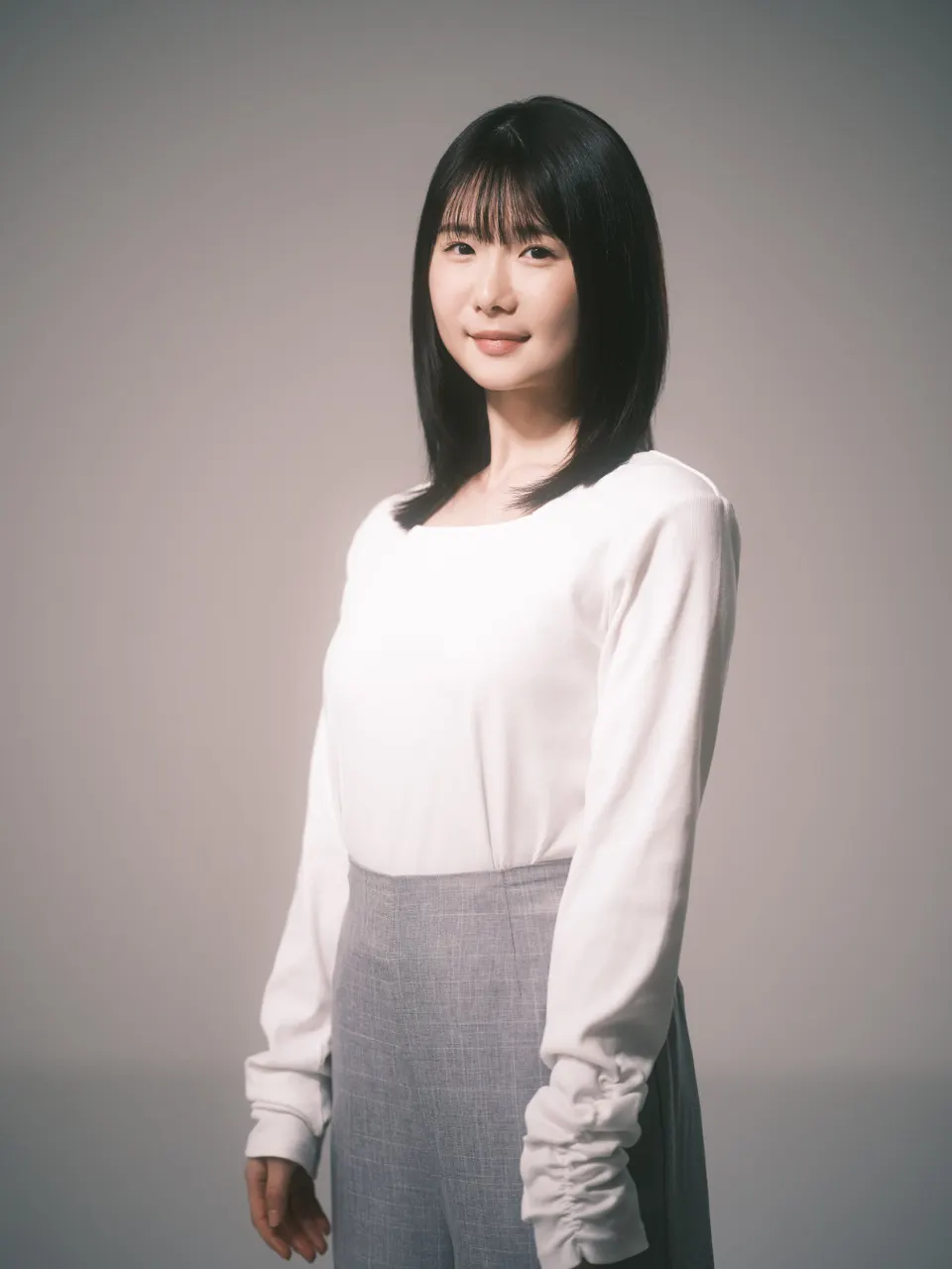 Karin Ono wearing a white long-sleeved top and gray skirt against a neutral studio background.