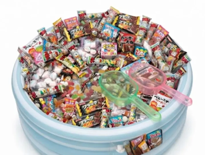 Illustrative sweets-scooping photograph showing packaged sweets in a round blue container with green and pink scoops.