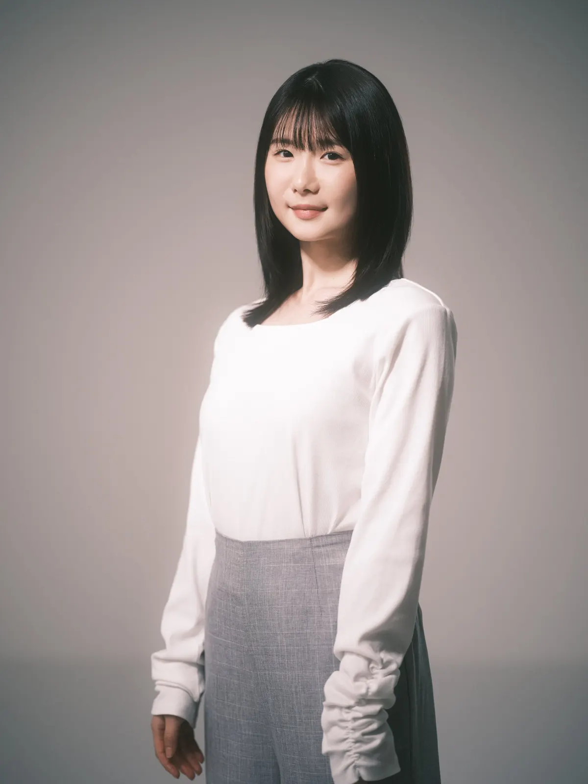 Karin Ono wears a white long-sleeved top and gray skirt against a neutral studio background.