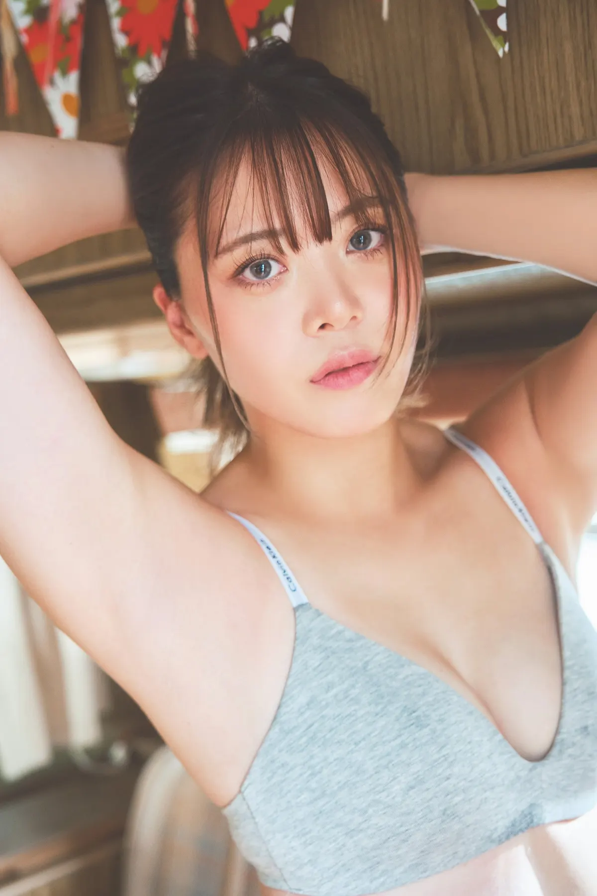 Mayu Iwatani (岩谷麻優) in a gray top with her arms raised behind her head against a wooden interior.