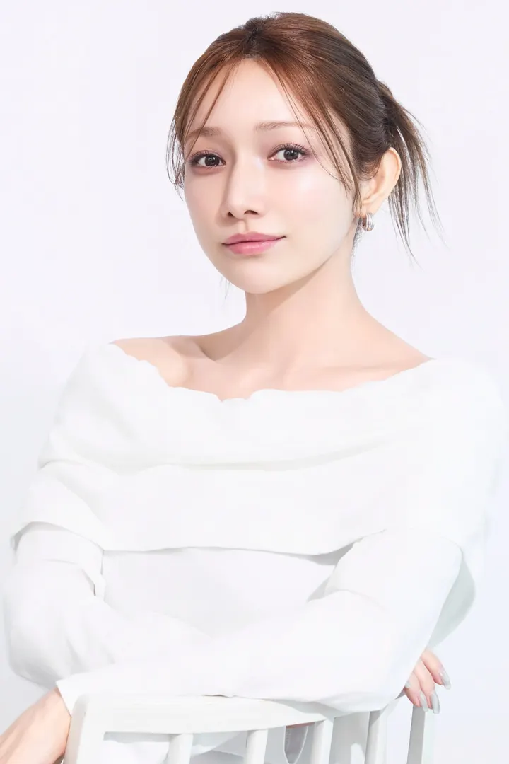 Maki Goto (後藤真希) in a white off-the-shoulder top, resting her arms on a white chair against a pale background.