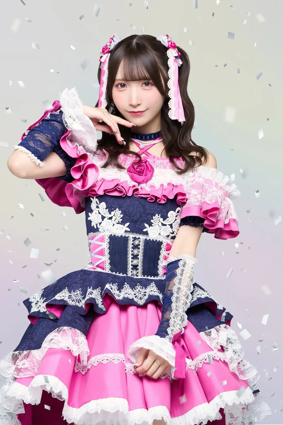 Shiori Kasai poses in a navy, white and pink ruffled stage costume with pink ribbons in her hair.