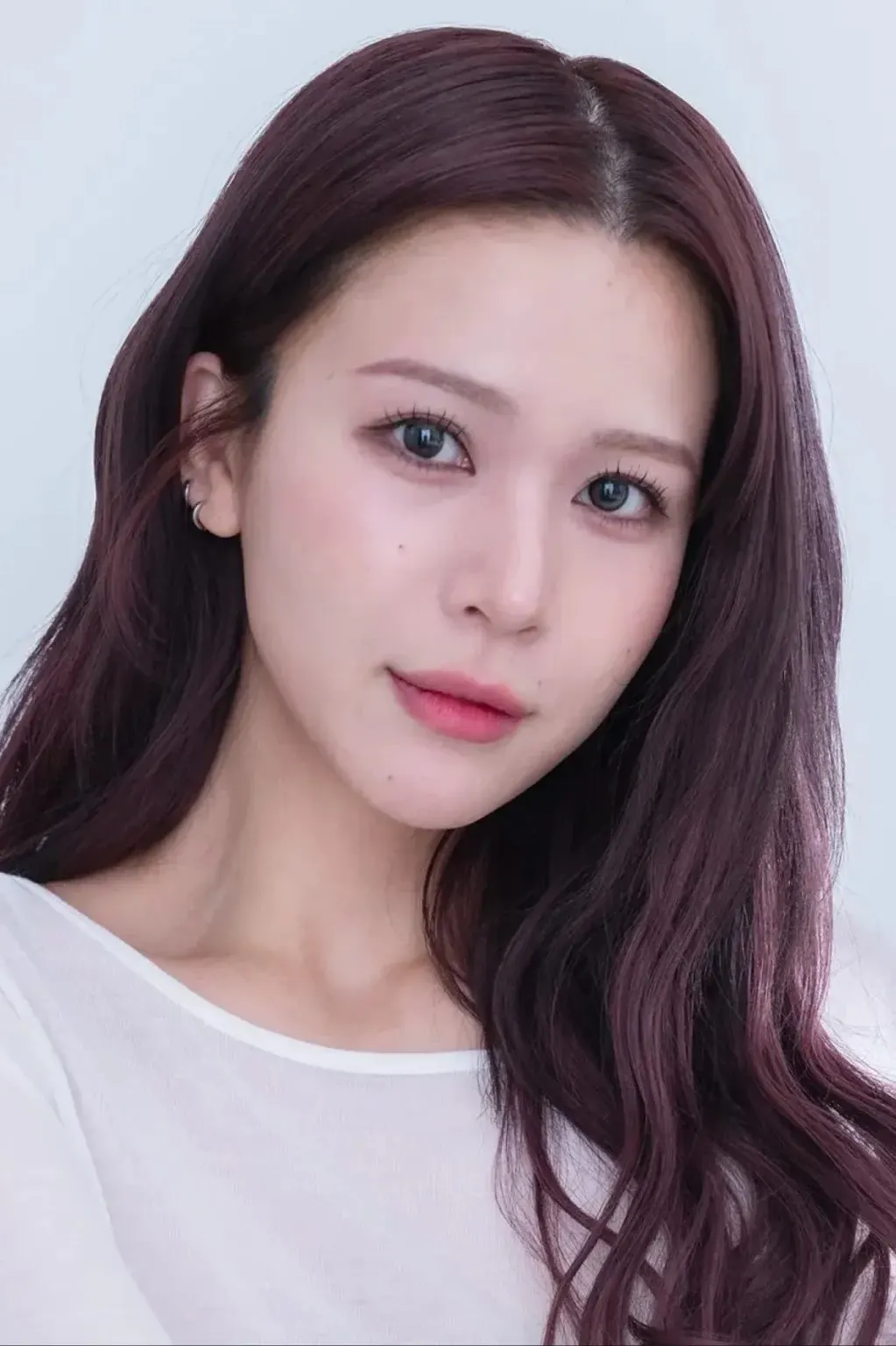Close portrait of AOI (あおい) with long reddish-brown hair and a white top against a pale background.