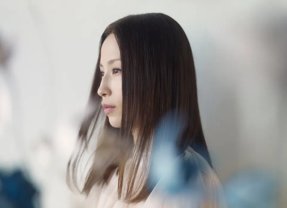 Uru in a light-colored blouse, with long straight brown hair, looking to the left against a softly blurred background.