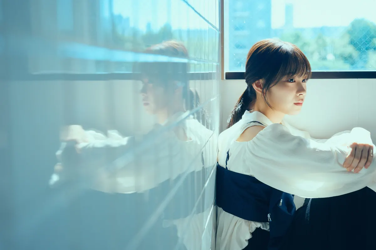 Wako Matsumoto seated beside a window, with her face and white blouse reflected in a pale blue tiled wall.
