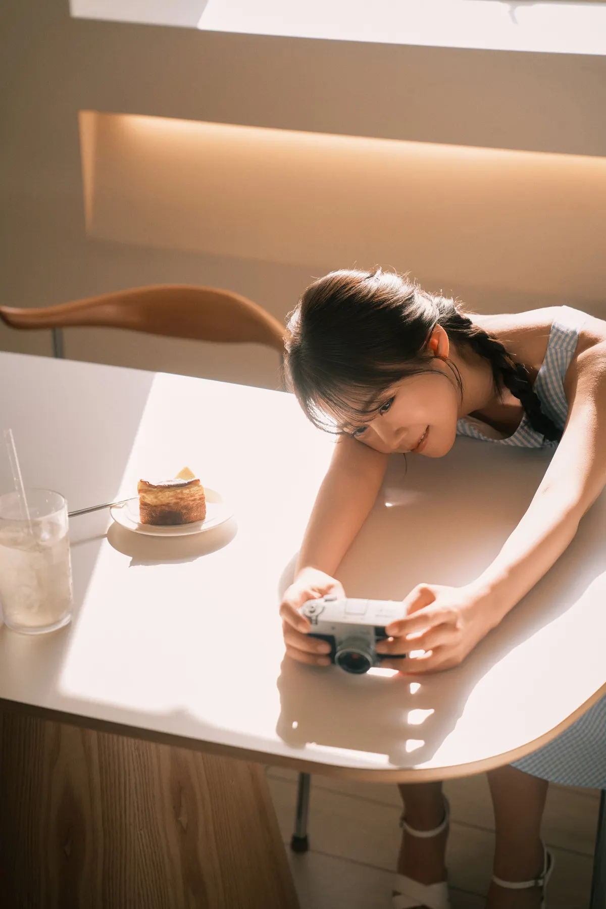 Han Seung Yeon (ハン・スンヨン) leans across a sunlit table holding a camera, with a drink and a slice of cake beside her.