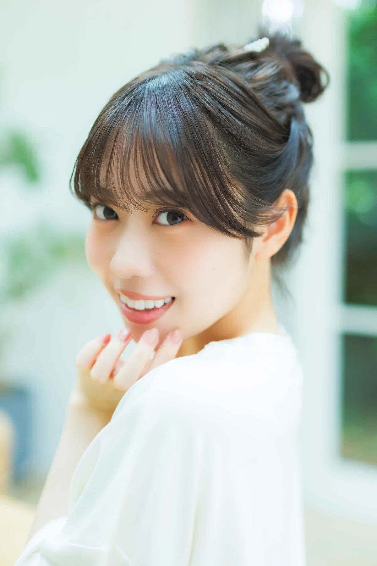 Sayuri Date smiles over her shoulder in a white top, with her hair tied up and fingertips near her chin, in an advance photograph for Love Voice 01.