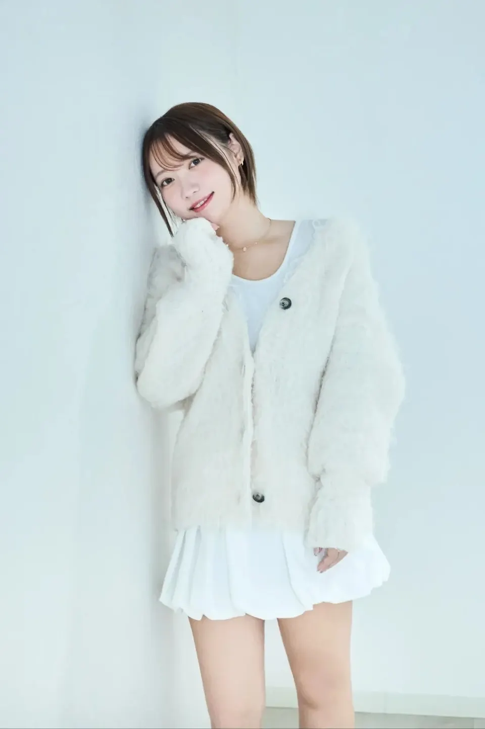 marichan(mogumuci) (まりちゃん(もぐむち)) standing against a pale wall in a fluffy white cardigan and white pleated skirt.