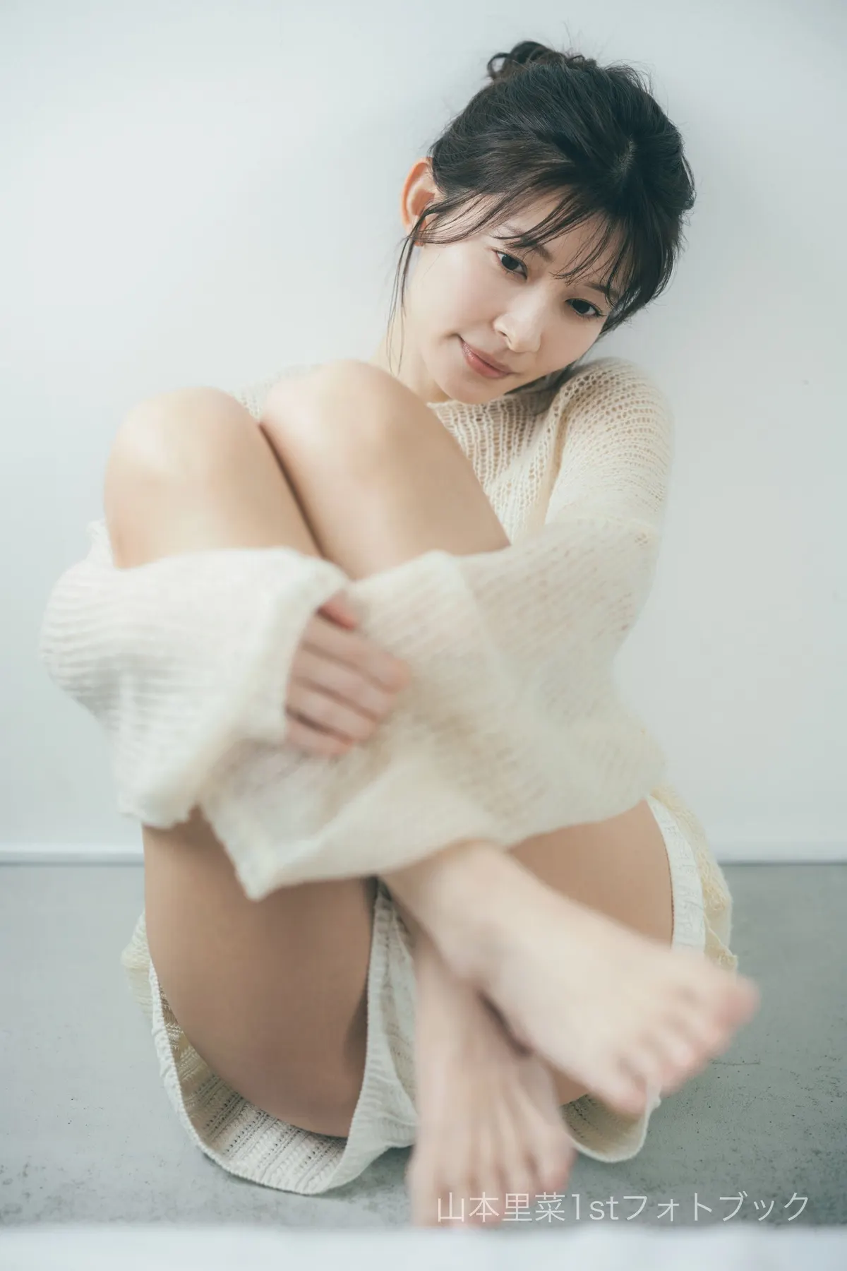 Rina Yamamoto (山本里菜) seated barefoot against a pale wall in cream open-knit clothing, holding her knees close.