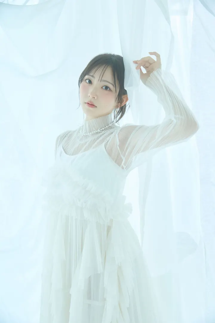 Nagisa Aoyama (青山なぎさ) in a white pleated outfit with sheer sleeves and a pearl-style necklace, raising one hand beside pale curtains.
