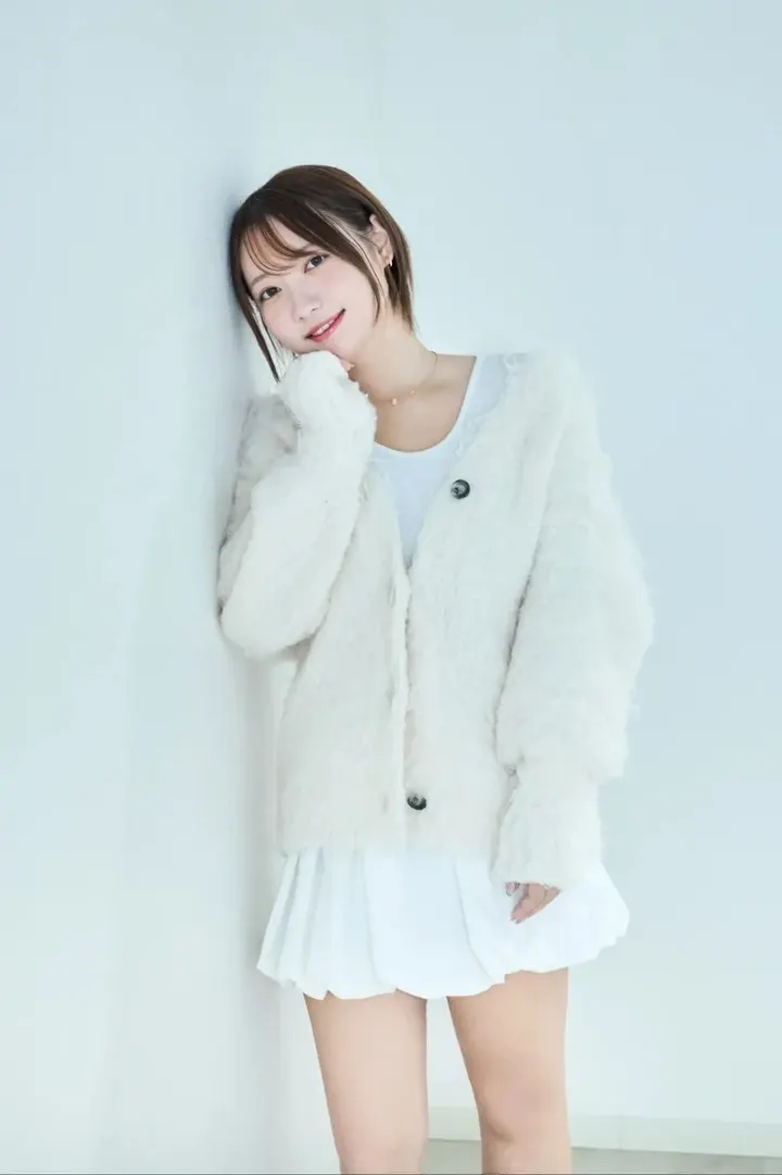 marichan(mogumuci) (まりちゃん(もぐむち)) standing against a pale wall in a fluffy white cardigan and white pleated skirt.