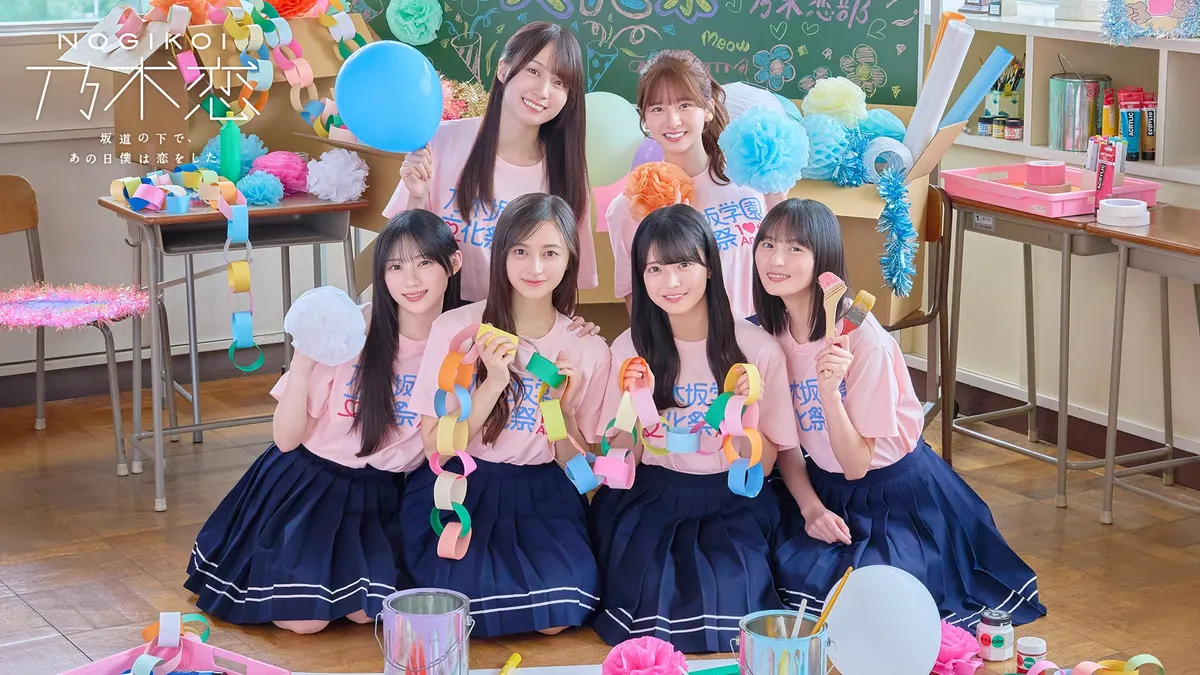 Six Cho! Nogikoi-bu members in pink festival T-shirts pose with paper chains, flowers and balloons in a decorated classroom.