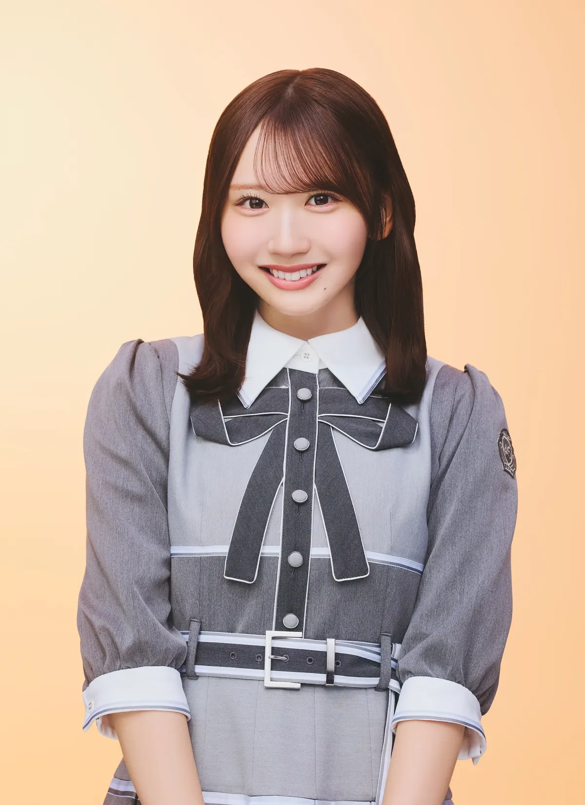Kaho Fujishima smiles in a gray belted outfit with a white collar and dark ribbon against a pale orange background.