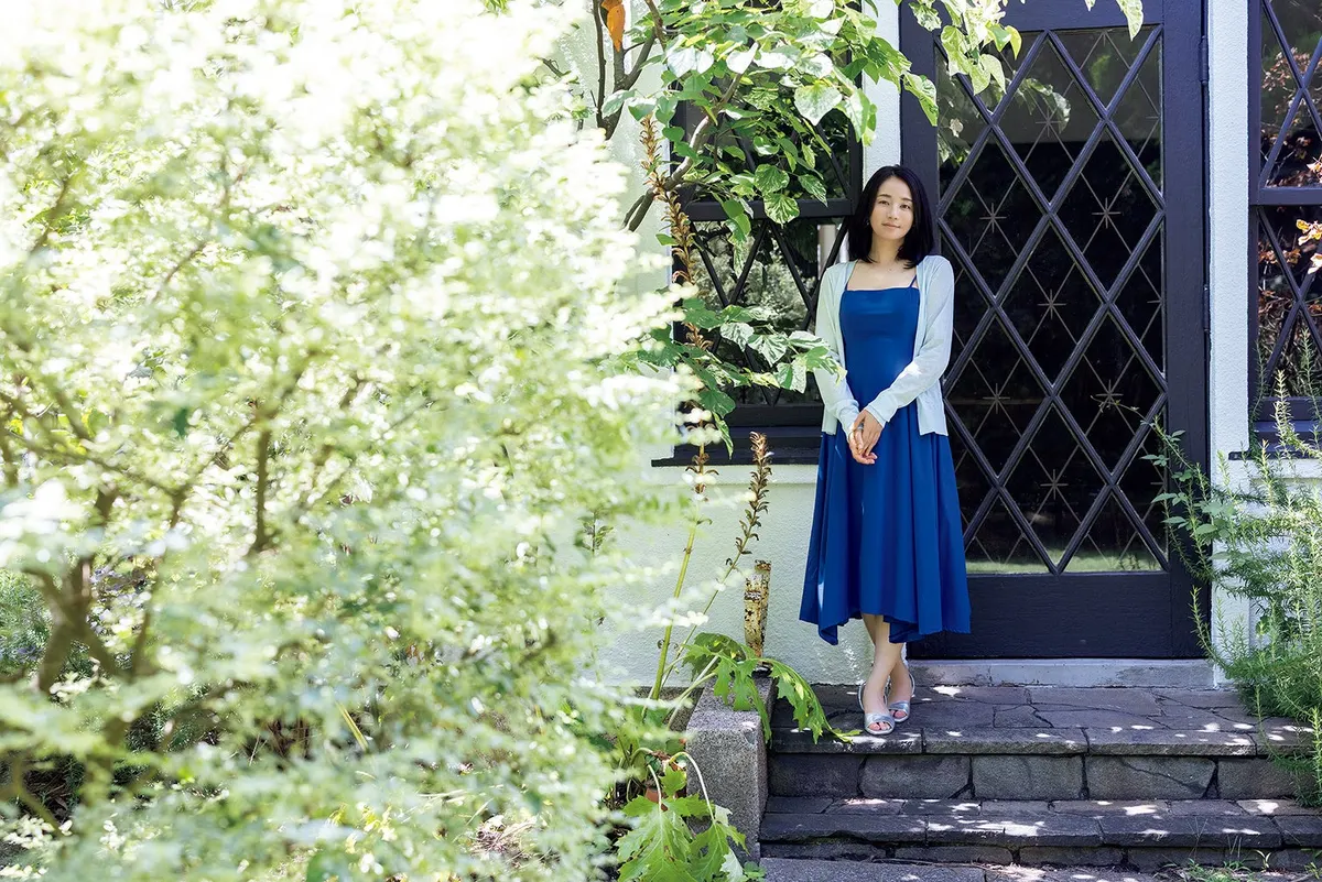 Fumino Kimura (木村文乃) in a blue dress and pale cardigan on stone steps outside diamond-paned doors, with greenery filling the left side.